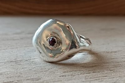 Ένα unisex δαχτυλίδι με γλυπτική, ακανόνιστη φόρμα και έναν κόκκινο λίθο στο κέντρο. Κατασκευασμένο σε ασήμι 925, με φυσικές καμπύλες που αγκαλιάζουν το δάχτυλο και διακριτική οργανική υφή. Ιδανικό για καθημερινή χρήση ή ως statement λεπτομέρεια.